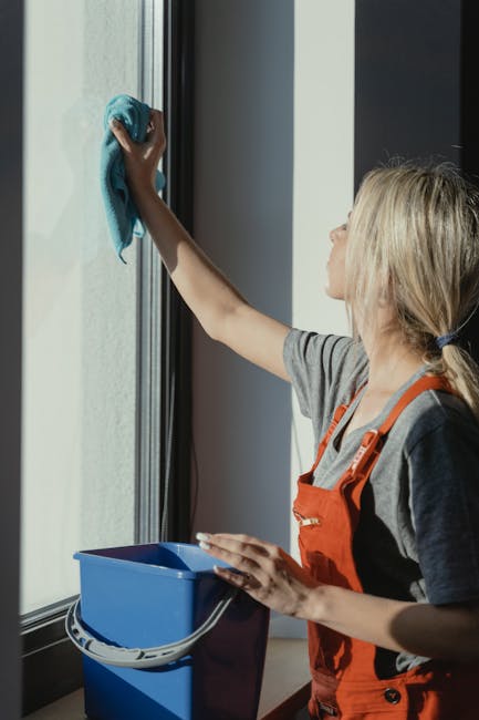 An arrangement of cleaning tools and supplies for surface cleaning and sanitisation in a bright, well-lit setting. There are pink rubber gloves at the top left corner, a pink cloth in the top right corner, and a translucent spray bottle in the bottom left corner. A pink and yellow sponge are positioned at the bottom center, with a white bottle of cleaning liquid on the right side. The surfaces and materials include smooth, shiny plastic, fabric, and sponge textures, indicating a focus on domestic cleaning. The overall cleanliness appears maintained, with no visible dust or dirt, reflecting professional deep cleaning practices. Lambeth Cleaner emphasizes thorough sanitisation for residential and commercial spaces, aligning with their focus on effective hygiene and surface care.