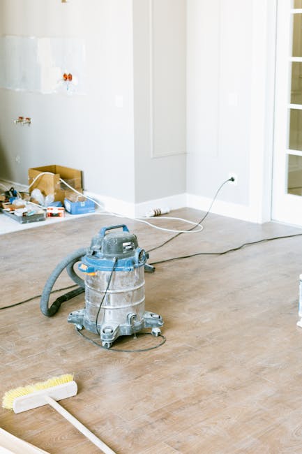 Two professional cleaners from Lambeth Cleaner are performing surface cleaning inside a modern, spacious kitchen following refurbishment. One cleaner is using a vacuum cleaner to ensure the tiled floo